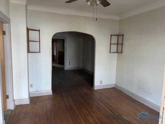 unfurnished room with arched walkways, ceiling fan, dark wood finished floors, and baseboards