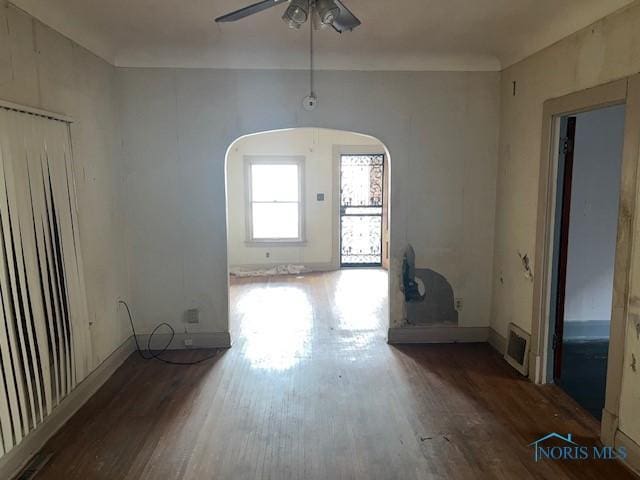 empty room with a ceiling fan, arched walkways, visible vents, and dark wood finished floors