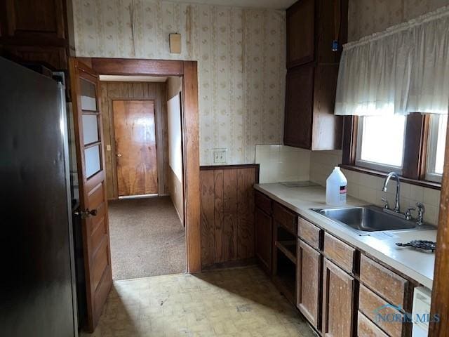 kitchen with a sink, light countertops, freestanding refrigerator, brown cabinetry, and wallpapered walls