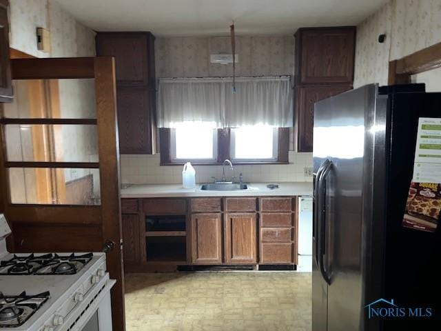 kitchen featuring light countertops, a sink, white gas range oven, stainless steel fridge, and wallpapered walls