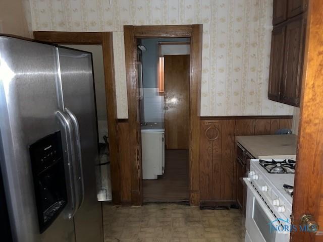 kitchen with white gas range, light countertops, wainscoting, stainless steel fridge with ice dispenser, and wallpapered walls