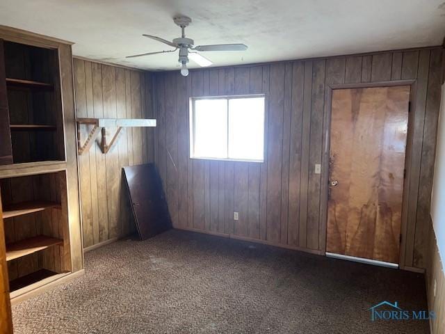 empty room featuring wood walls, dark carpet, and a ceiling fan