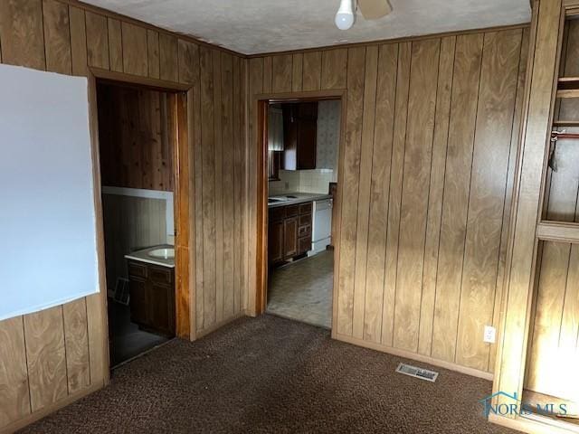 empty room with wood walls, visible vents, dark carpet, and a ceiling fan