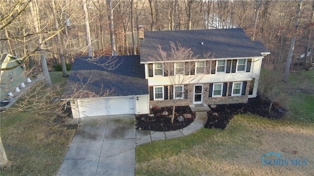 colonial house with an attached garage, a chimney, driveway, and a shingled roof