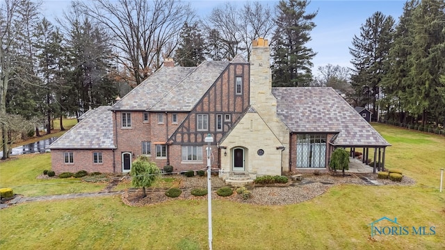 tudor home featuring a front lawn, a chimney, and a high end roof