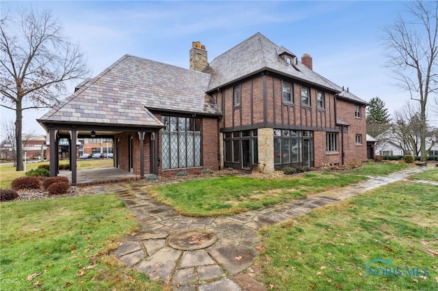 back of property with a yard, a high end roof, a chimney, and brick siding