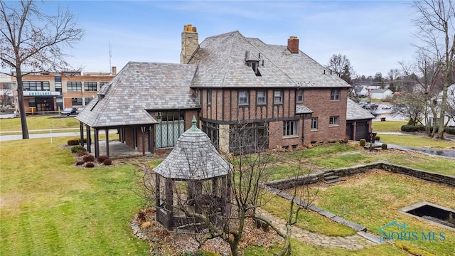 rear view of house with a high end roof, brick siding, a lawn, and a chimney