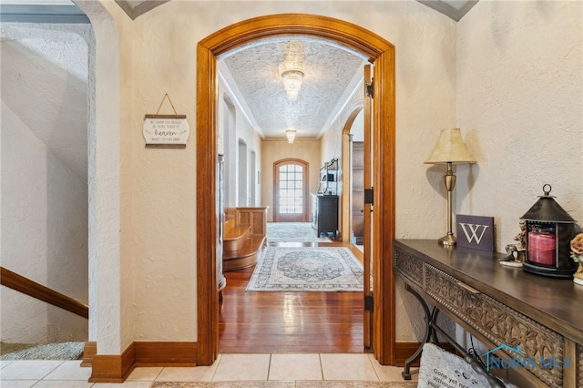 hallway featuring ornamental molding, arched walkways, a textured wall, and light tile patterned floors