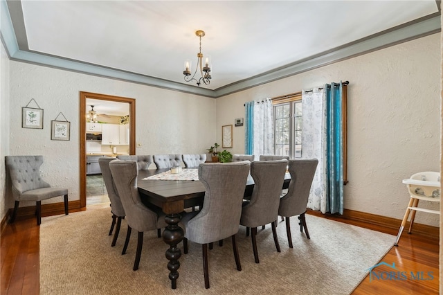 dining area with an inviting chandelier, crown molding, wood finished floors, and a textured wall