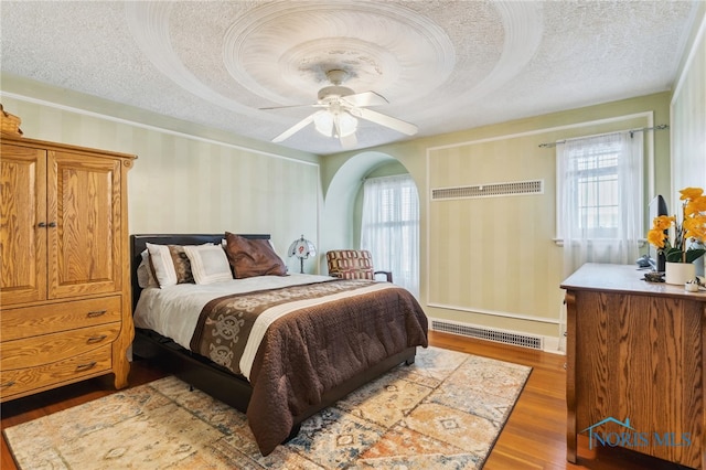 bedroom featuring visible vents, a textured ceiling, multiple windows, and wood finished floors