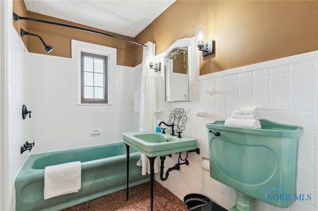 bathroom featuring tile walls, shower / tub combo, wainscoting, a sink, and a textured ceiling