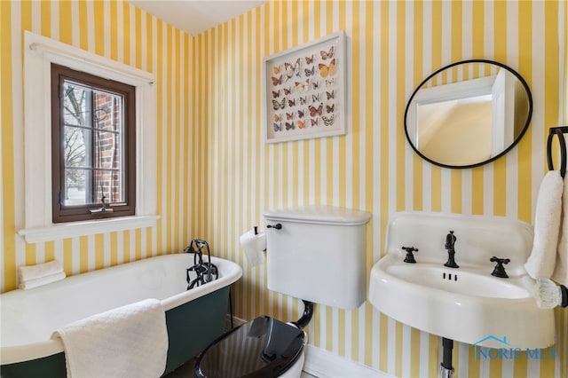 full bathroom featuring a soaking tub, a sink, toilet, and wallpapered walls