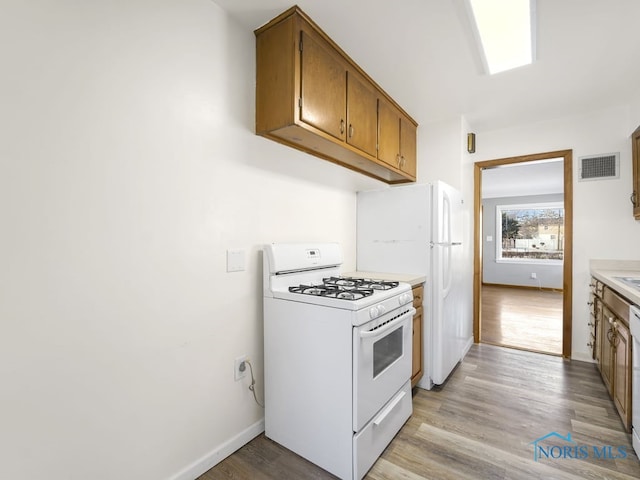 kitchen with light countertops, visible vents, light wood-style flooring, brown cabinetry, and white appliances