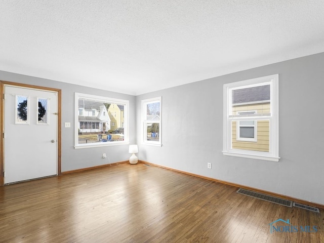 interior space with a textured ceiling, wood finished floors, visible vents, and baseboards