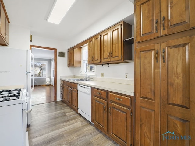 kitchen featuring white appliances, brown cabinetry, light wood-style flooring, light countertops, and a sink