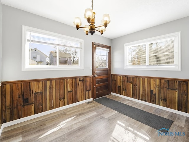 unfurnished dining area with a wainscoted wall, wood finished floors, an inviting chandelier, and wood walls