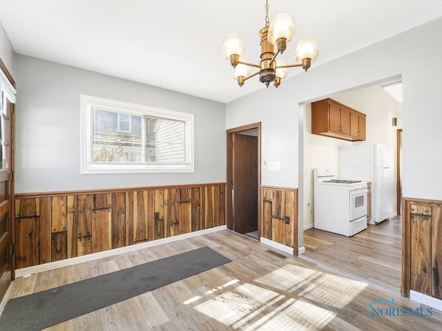 kitchen with wooden walls, wainscoting, brown cabinetry, white gas range, and decorative light fixtures