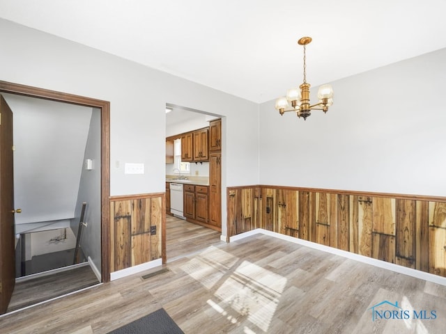 unfurnished dining area featuring light wood-style flooring, wainscoting, a sink, and visible vents