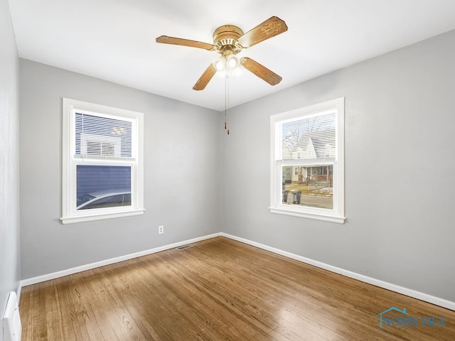 empty room featuring a ceiling fan, wood finished floors, visible vents, and baseboards