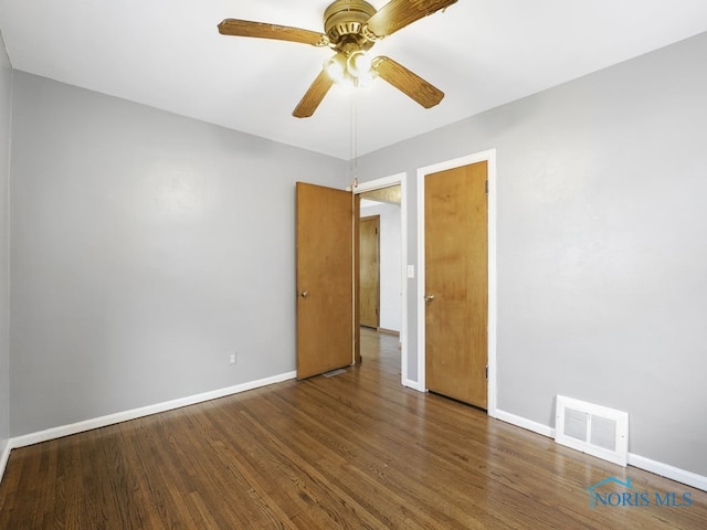 spare room featuring baseboards, visible vents, ceiling fan, and dark wood-type flooring