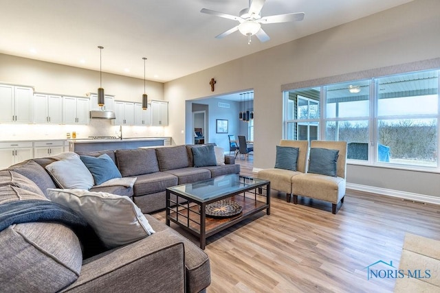 living area with visible vents, light wood-type flooring, a ceiling fan, and baseboards