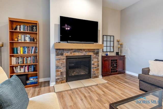 living room featuring light wood finished floors, baseboards, and a stone fireplace