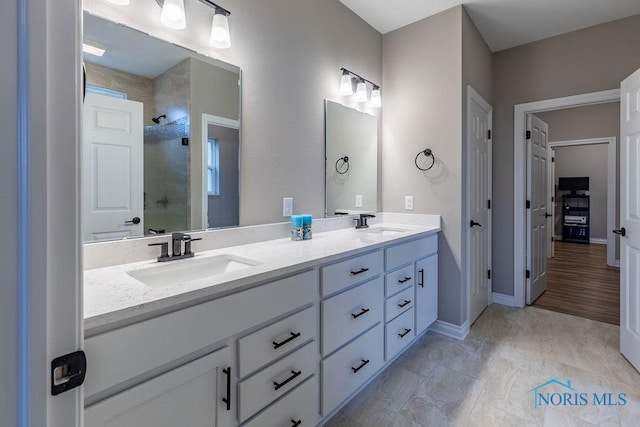 bathroom with double vanity, baseboards, a sink, and tiled shower