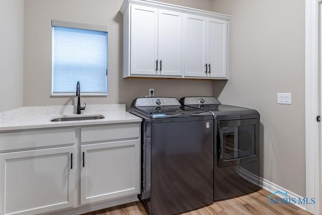 laundry area featuring cabinet space, baseboards, light wood-style flooring, independent washer and dryer, and a sink