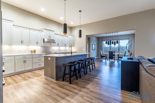 kitchen featuring decorative light fixtures, light countertops, open floor plan, white cabinetry, and a kitchen island with sink