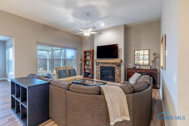 living area with a ceiling fan, baseboards, wood finished floors, and a stone fireplace