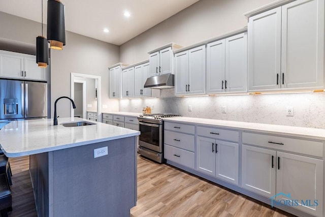 kitchen featuring under cabinet range hood, a sink, appliances with stainless steel finishes, tasteful backsplash, and a center island with sink