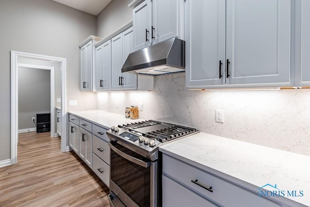 kitchen featuring light stone counters, stainless steel range with gas stovetop, light wood-type flooring, under cabinet range hood, and backsplash