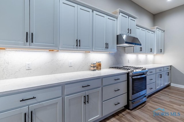 kitchen featuring backsplash, gas stove, light wood-type flooring, under cabinet range hood, and baseboards