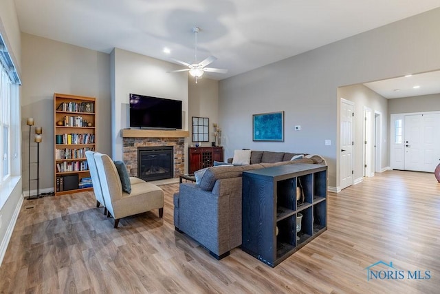 living room with ceiling fan, a stone fireplace, baseboards, and wood finished floors