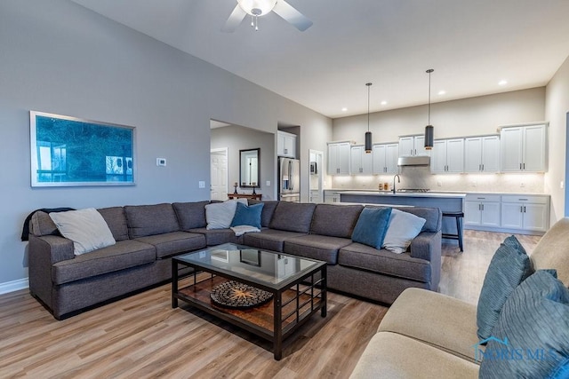 living area featuring baseboards, light wood finished floors, a ceiling fan, and recessed lighting