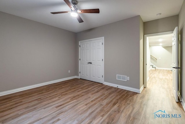 unfurnished bedroom featuring light wood finished floors, visible vents, baseboards, ceiling fan, and a closet