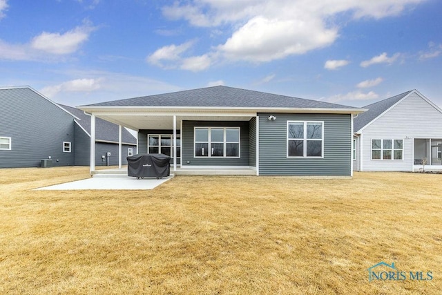 back of property with a yard, a shingled roof, and a patio area