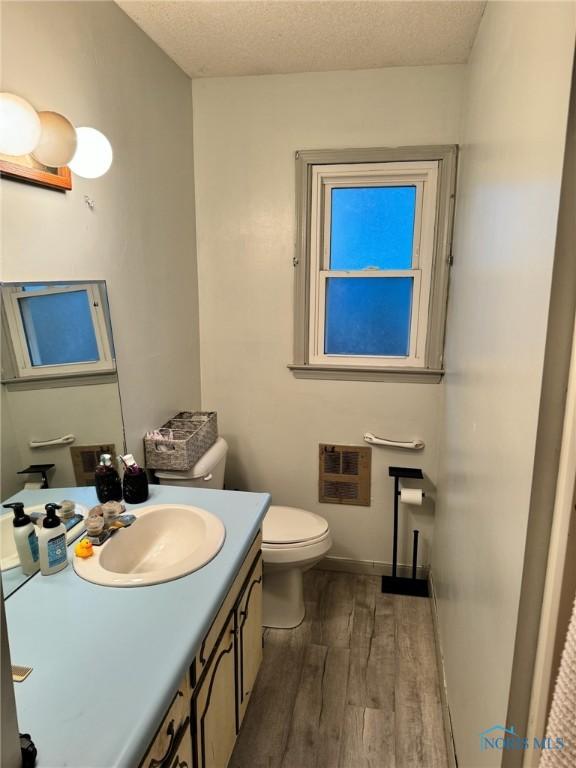 bathroom with toilet, a textured ceiling, vanity, wood finished floors, and baseboards