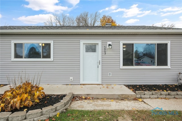 view of exterior entry featuring a patio and roof with shingles