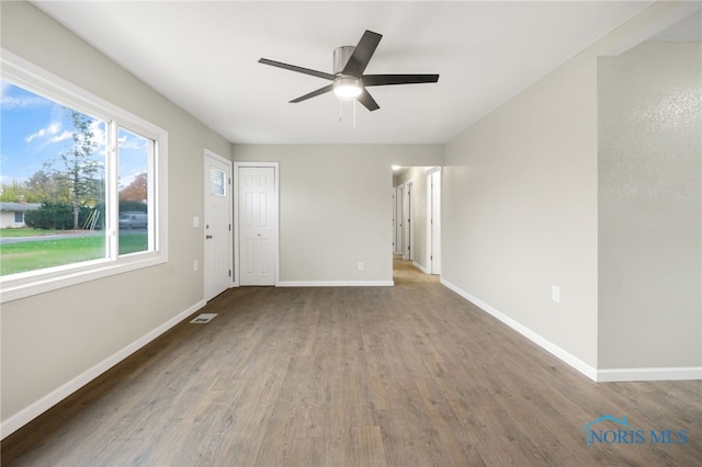 unfurnished living room with ceiling fan, dark wood-type flooring, visible vents, and baseboards