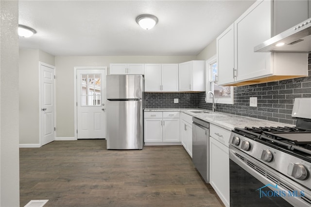 kitchen featuring a sink, white cabinetry, appliances with stainless steel finishes, decorative backsplash, and wall chimney exhaust hood