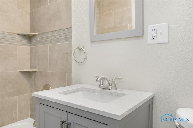 full bathroom with a textured wall, vanity, and toilet