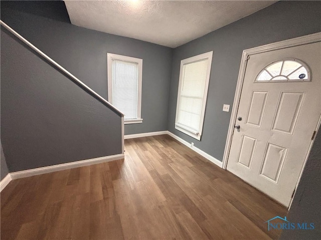 entryway featuring stairs, a textured ceiling, baseboards, and wood finished floors