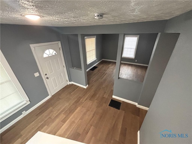 entrance foyer featuring baseboards, a textured ceiling, visible vents, and wood finished floors