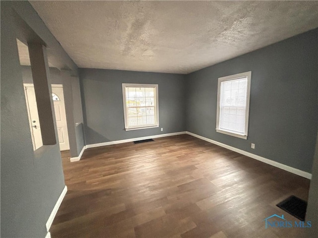 spare room with baseboards, a textured ceiling, visible vents, and wood finished floors