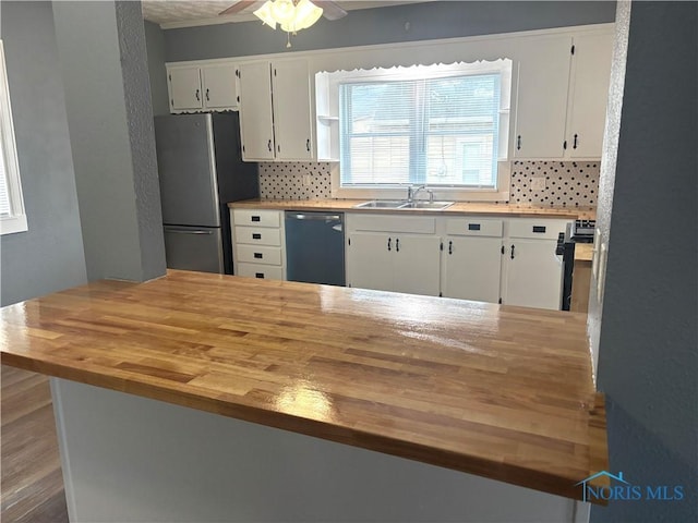 kitchen with butcher block counters, decorative backsplash, freestanding refrigerator, a sink, and dishwasher