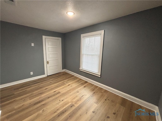 empty room with a textured ceiling, wood finished floors, and baseboards