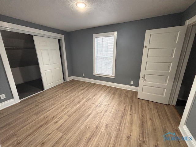 unfurnished bedroom with a closet, a textured ceiling, baseboards, and wood finished floors