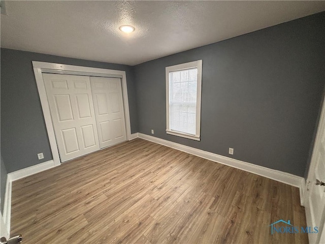 unfurnished bedroom with a textured ceiling, a closet, wood finished floors, and baseboards