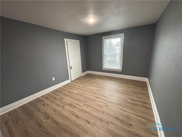 spare room featuring a textured ceiling, baseboards, and wood finished floors